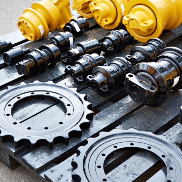 Assorted industrial machinery parts, including gears, rollers, and drive components, laid out on a black wooden pallet.